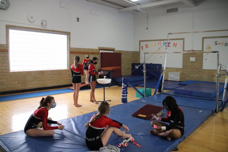 Members sit on the mat relaxing, as their teammates prepare to attempt a skill. The coaches hope the girls complete skills they have been working on. 