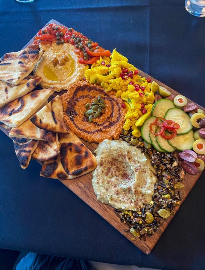 The Mezze Platter served on a wooden cutting board features three different dips, pickled vegetables and pita bread.