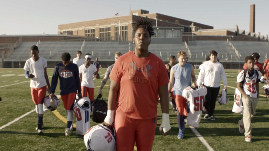 Piarus Walker, backed by his Messwood teammates, holds a helmet with bleachers in the background. Piarus is one of the featured students in the "Messwood" film.